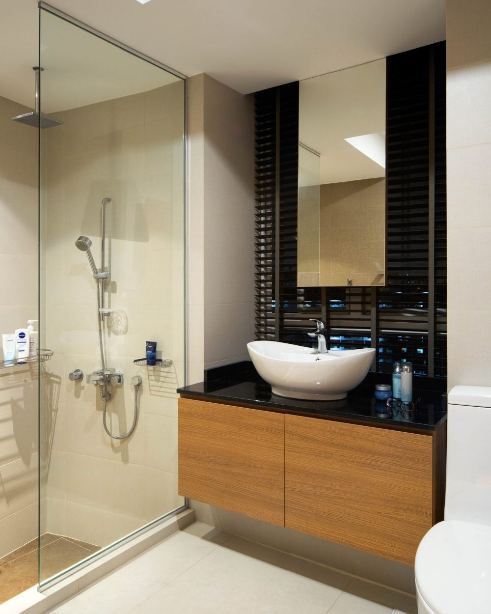 A timber vanity with a black stone counter and vessel sink pairs with a glass-enclosed shower, finished with a patterned screen for privacy.