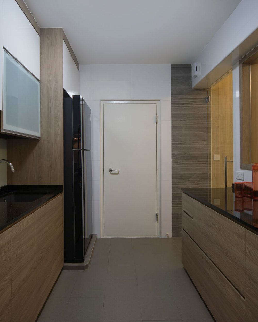 Warm timber lower cabinets pair with crisp white uppers and a glass-panelled sliding door, keeping the galley kitchen bright and contained.