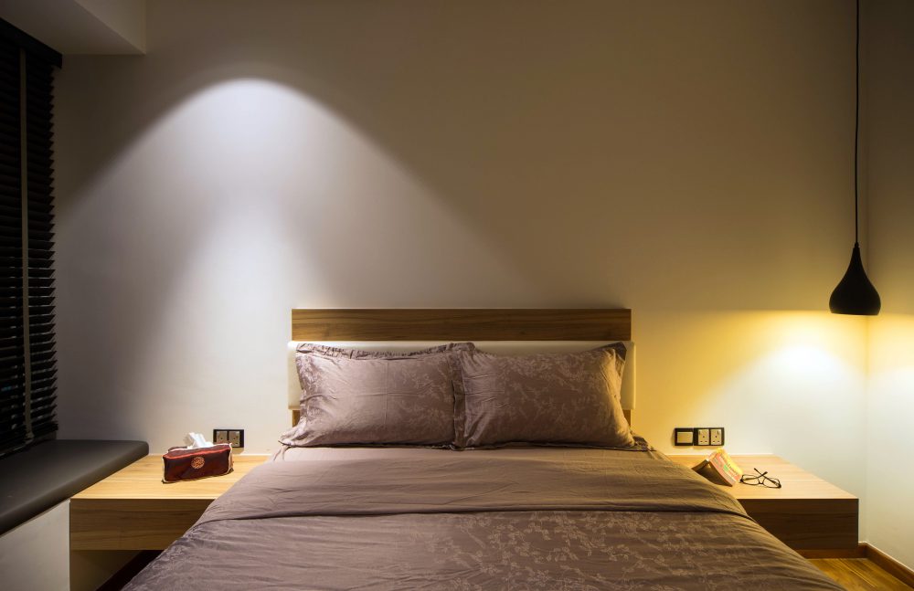 A solid timber headboard is flanked by hanging pendant lights on either side, keeping the bedroom's lighting soft and layered.
